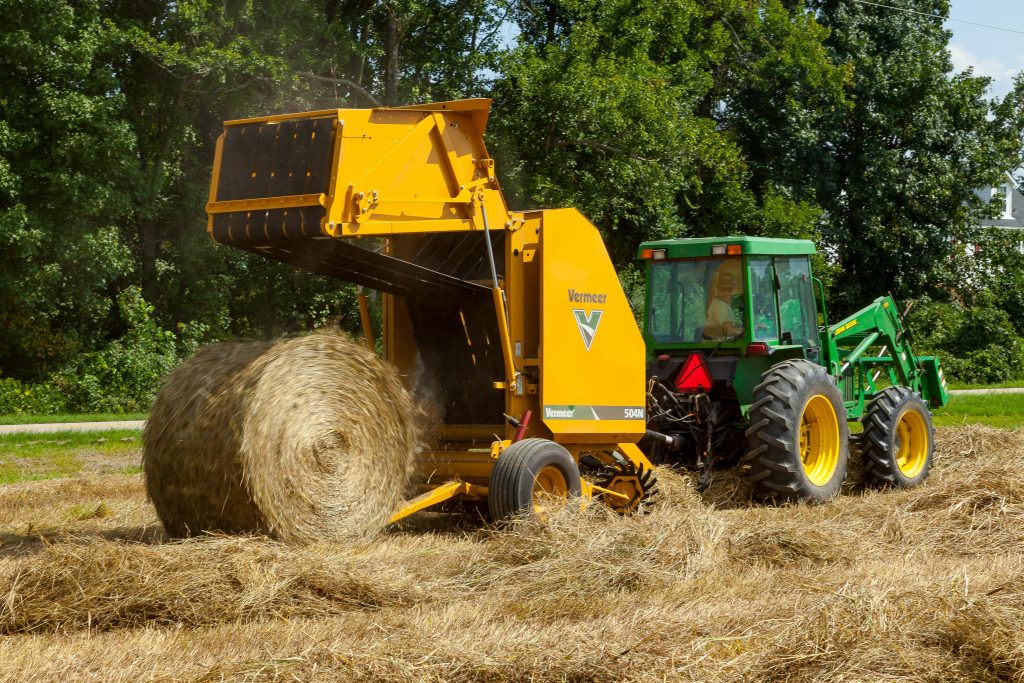 pexels-photo-2965670-2965670 A tractor and baler machine working together to form a hay bale in a sunny field.